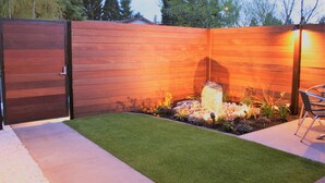 Une clôture en bois avec un portail, une pelouse bien entretenue et un petit jardin agrémenté de rochers et de plantes.