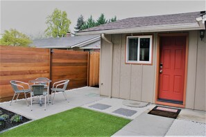 A small shed with a red door, a window, and a doorbell. There is a patio with two chairs and a small table. - Relax & Enjoy Private Studio w/Courtyard (Eugene)