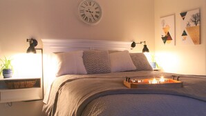 Un lit bien fait, avec une tête de lit, des lampes de chevet, une horloge et des œuvres d’art accrochées au mur.