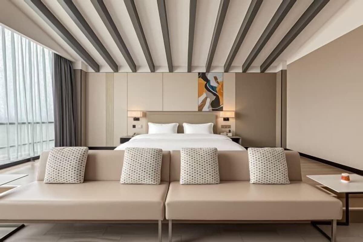 A modern hotel room with a large bed, two sofas, a nightstand, and a painting on the wall.