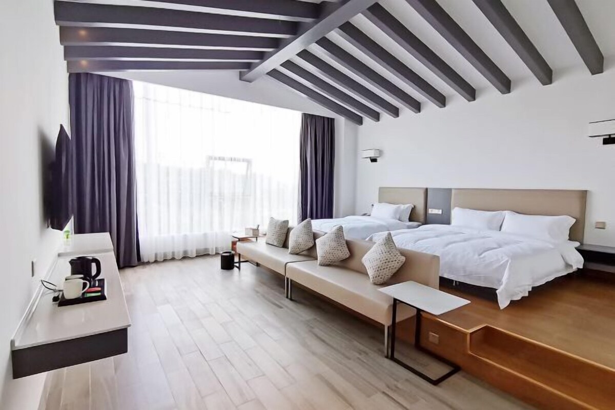A modern hotel room with a large bed, a seating area, a flat-screen TV, and a wooden floor.