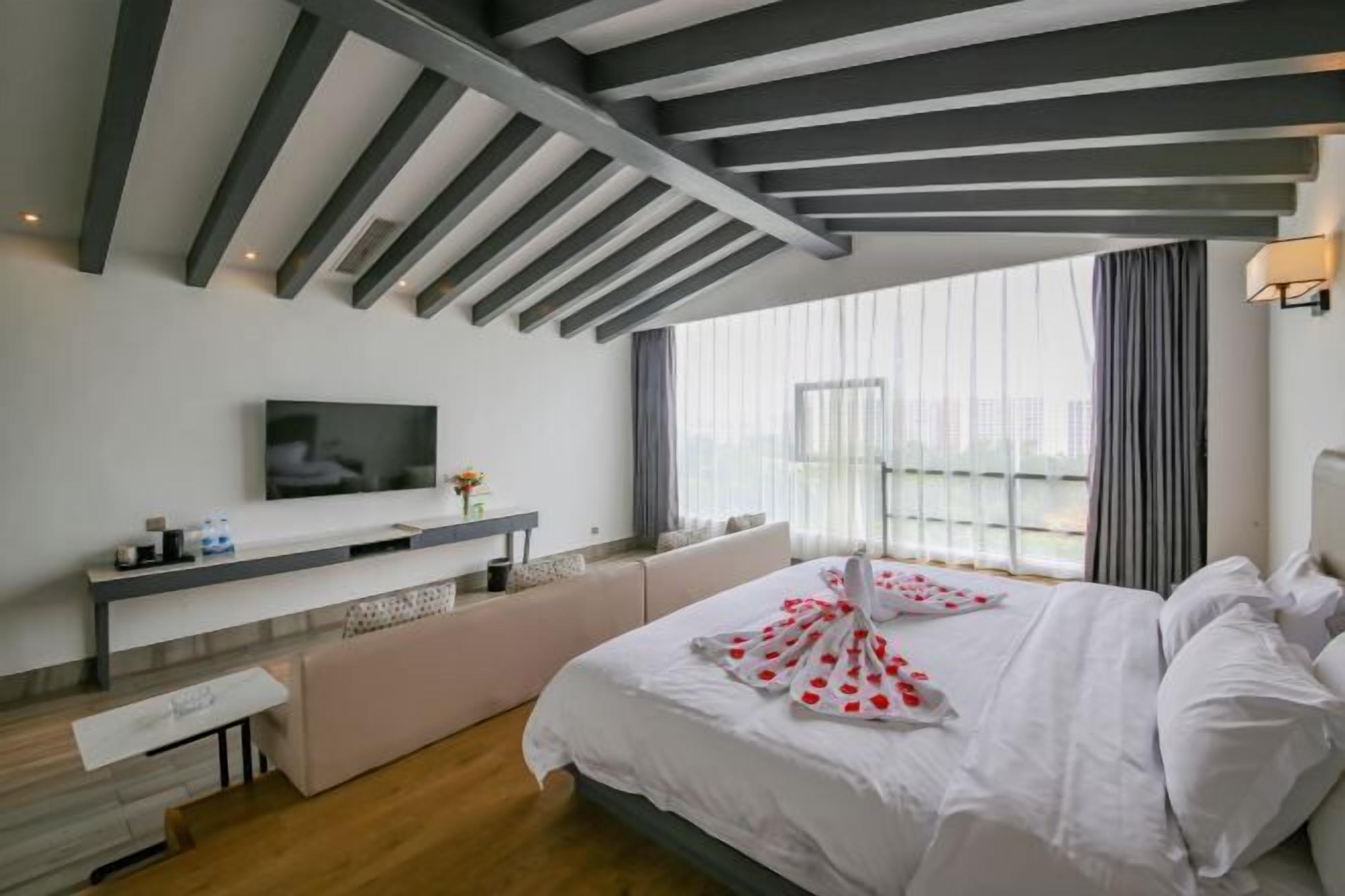 A modern hotel room with a large bed, a flat-screen TV, a bedside table, and a window with curtains.