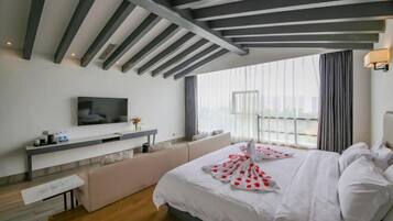 A modern hotel room with a large bed, a flat-screen TV, a bedside table, and a window with curtains.