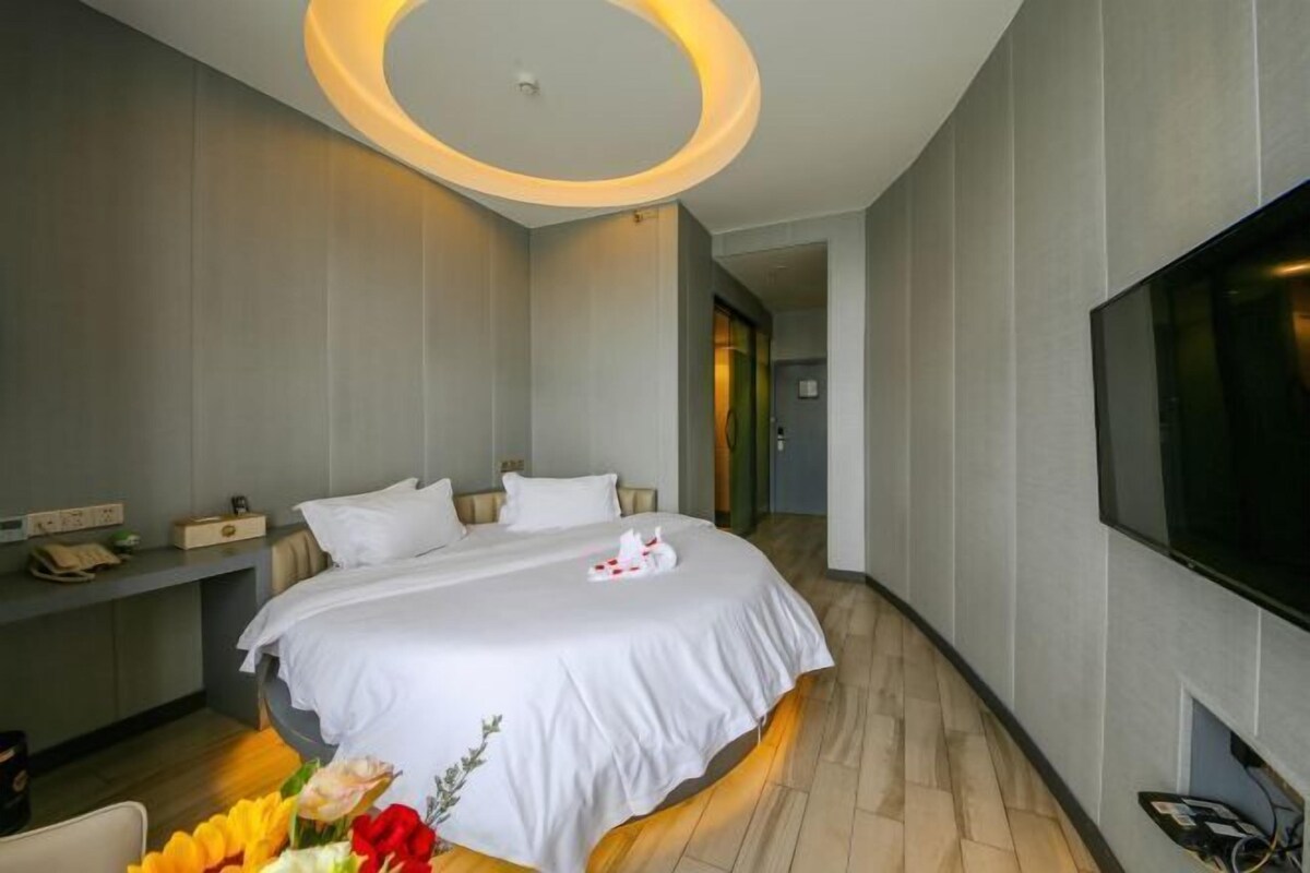 A modern hotel room with a large bed, a flat-screen TV, and a wooden floor.