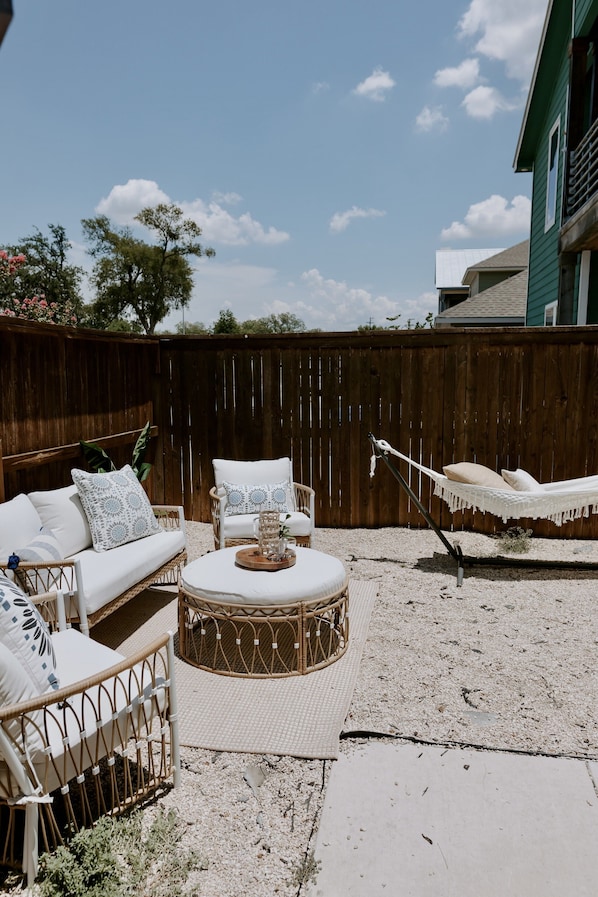 A backyard with a wicker sofa, a round table, and a hammock.