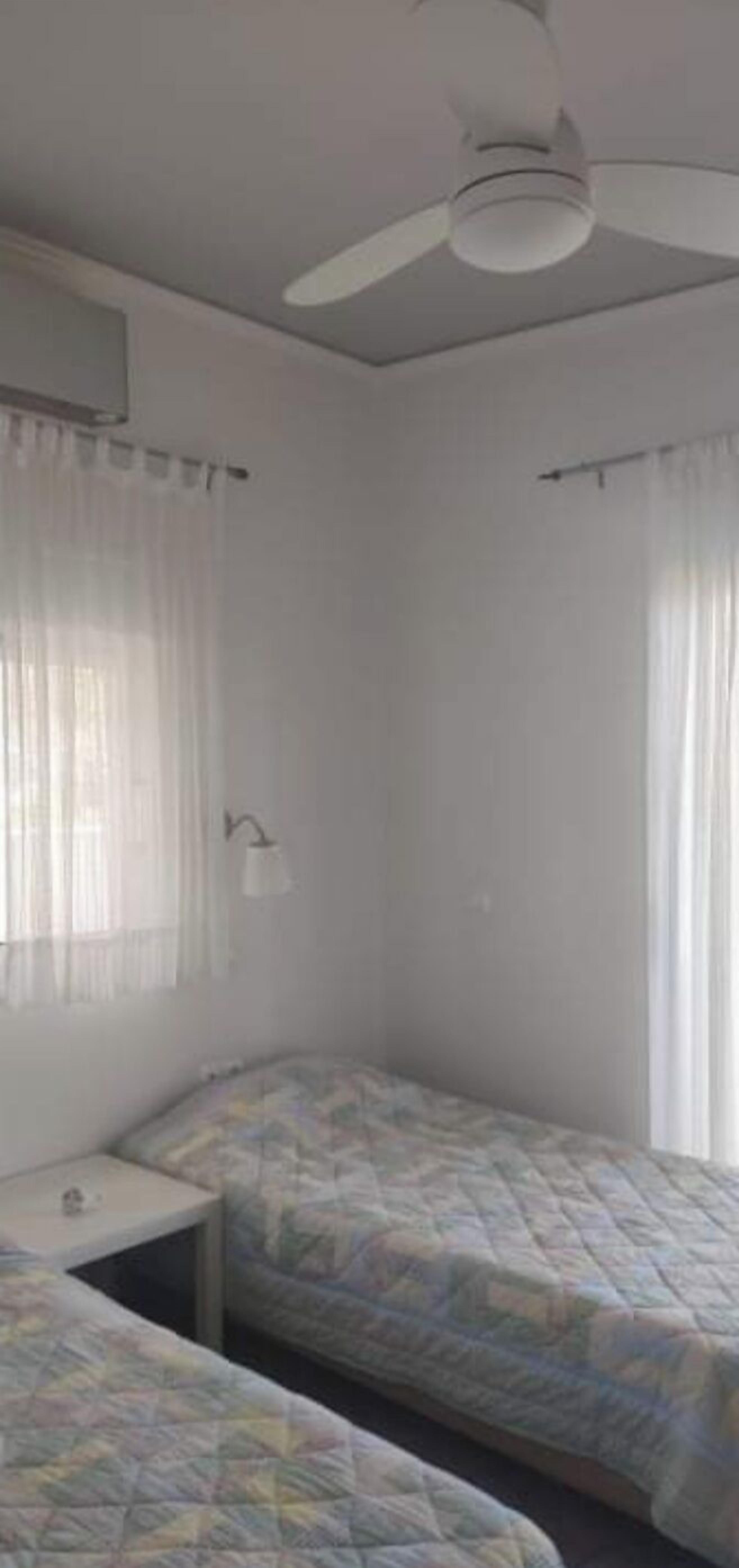 Une chambre avec deux lits, un ventilateur de plafond et une fenêtre avec des rideaux.