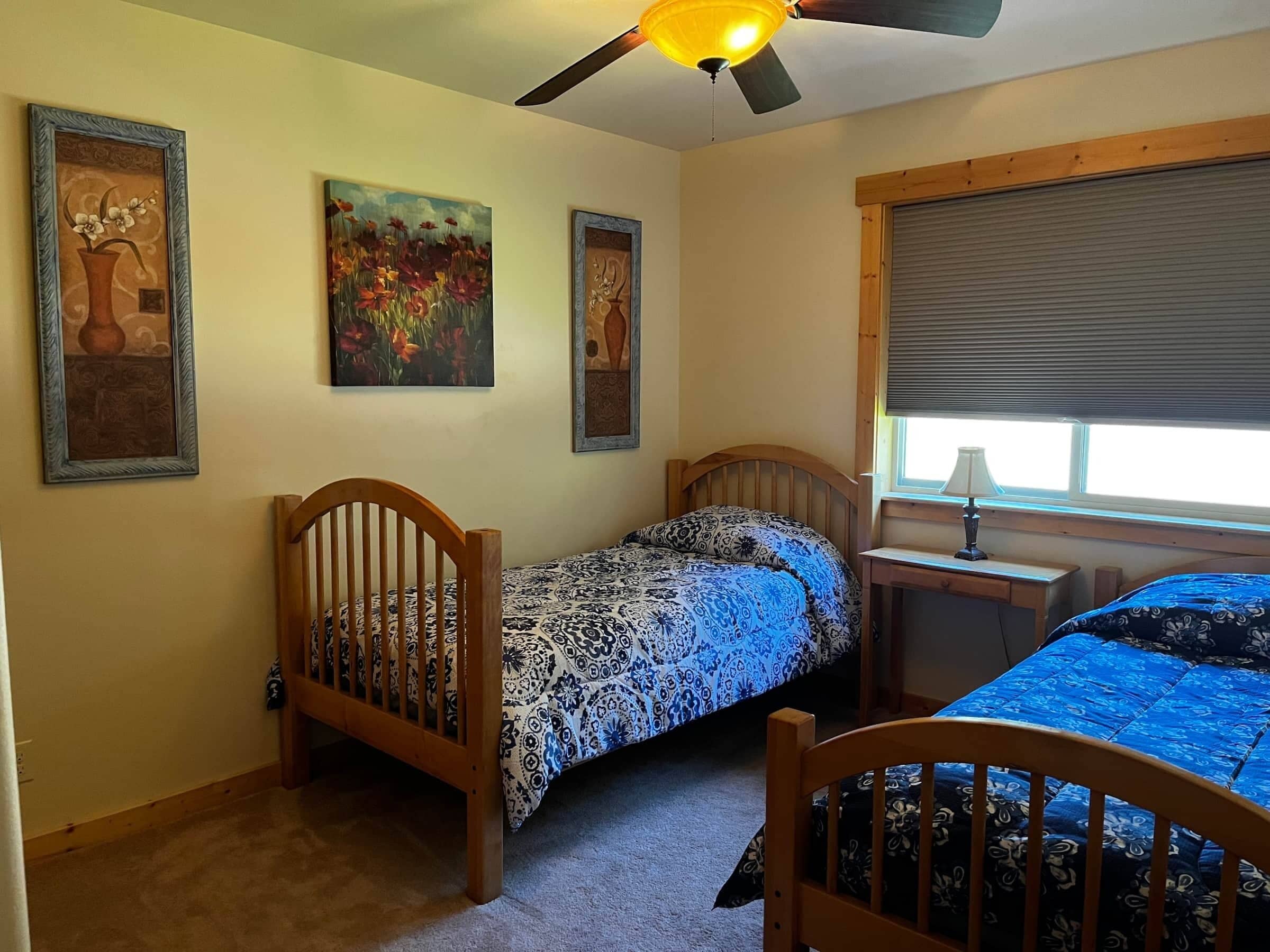Un dormitorio con dos camas individuales, un ventilador de techo y tres cuadros en la pared.