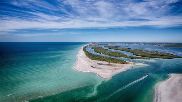 Vue aérienne d’une zone côtière avec des eaux d’un bleu limpide, des plages de sable et une petite île couverte de végétation.