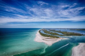 Vue aérienne d’une zone côtière avec des eaux d’un bleu limpide, des plages de sable et une petite île couverte de végétation.
