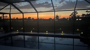 Une piscine intérieure moderne dotée d’un toit en verre, offrant une vue sur un coucher de soleil se déclinant sur un paysage rural.