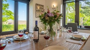 Mesa de comedor dispuesta para cuatro personas, con copas de vino, una botella de vino y un jarrón de flores.
