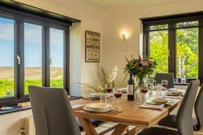 Un coin repas avec une table en bois dressée pour quatre personnes, de grandes fenêtres et un panneau accroché au mur.