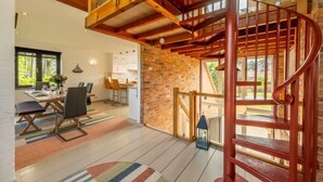 Un interior moderno con una escalera de madera, un comedor con mesa y sillas, y vistas al exterior.