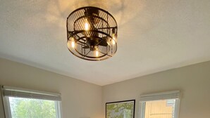 Une chambre à coucher avec un grand lit, deux tables de chevet, un luminaire au plafond et deux fenêtres.