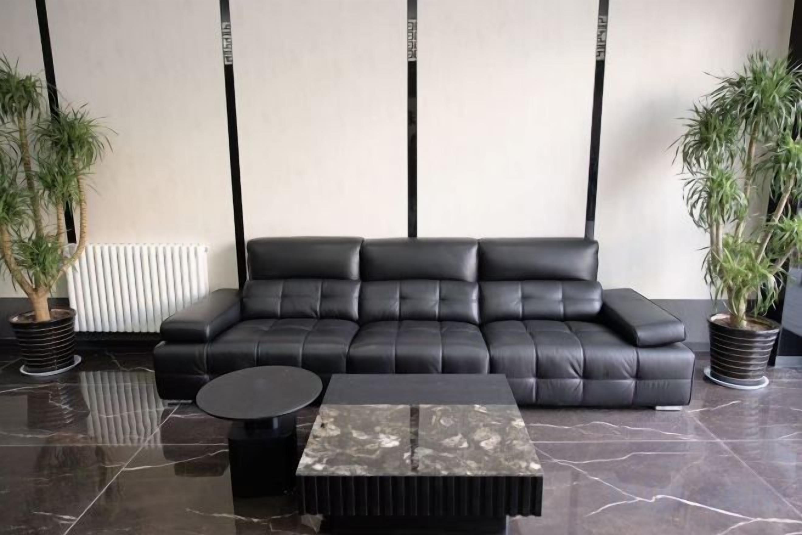 A modern living room with a black leather sofa, a marble coffee table, and two potted plants.