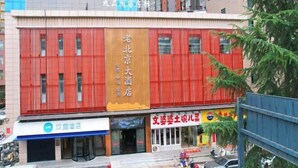 Un bâtiment doté d’une façade rouge imposante, d’une enseigne indiquant « 老北京大酒店 » et d’une devanture de magasin avec une enseigne indiquant « 文塑陶瓷儿童 ».