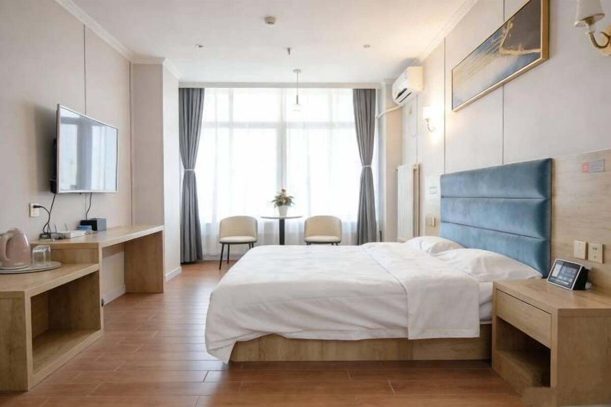 Une chambre d’hôtel avec un lit, des tables de chevet, une télévision, un bureau et une fenêtre avec des rideaux.