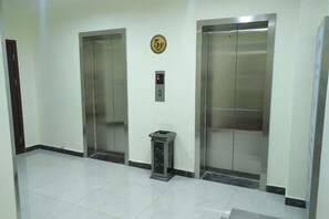 Un espace ascenseur propre et moderne, comprenant deux ascenseurs, un panneau de commande et une petite poubelle.
