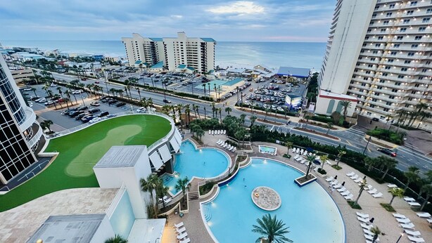 A resort with a large swimming pool, multiple lounge areas, and a view of the ocean.