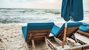 A beach with wooden lounge chairs and a blue umbrella.
