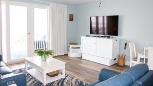 A living room with a TV, white furniture, a ceiling fan, and a view through a sliding door.
