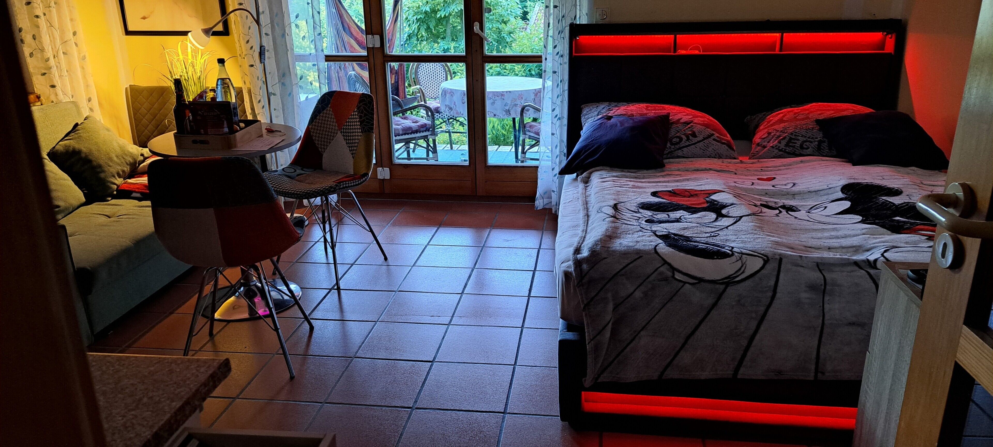 A bedroom with a bed, a chair, a table, and a view of the outdoors.