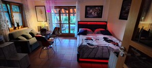 Un dormitorio con cama, sofá, sillón, mesa y ventana con cortinas.