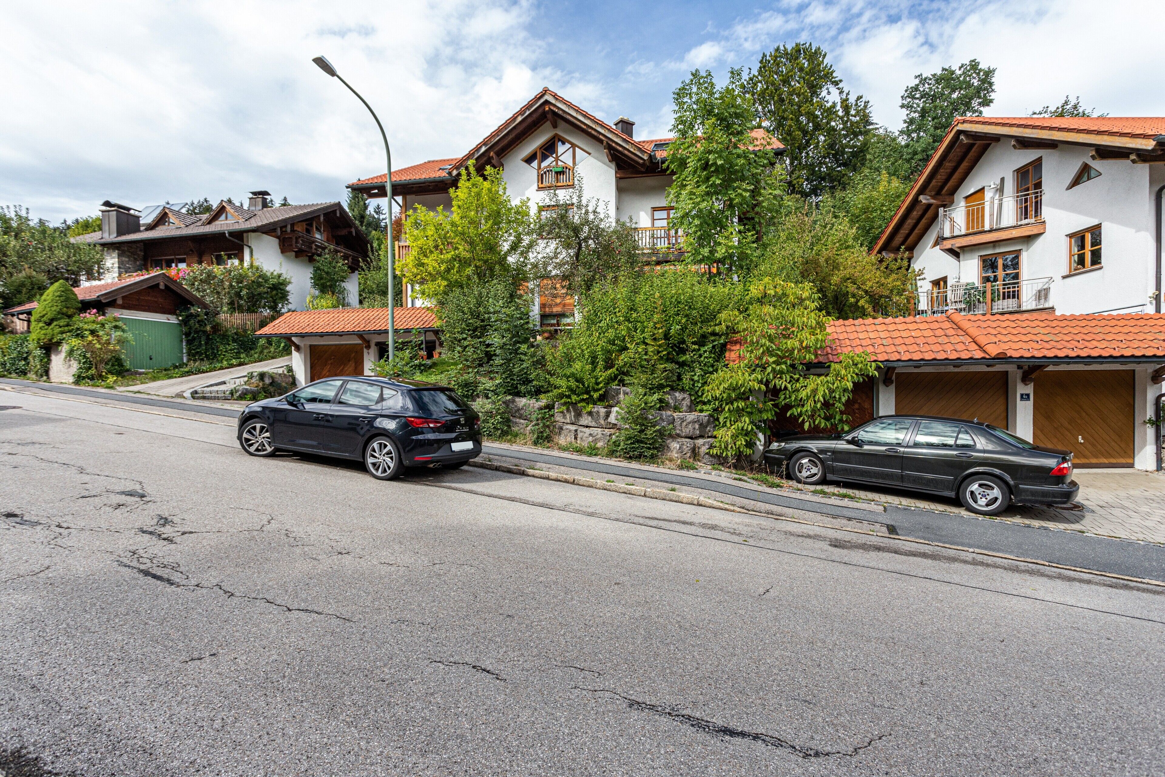 A residential building with a red-tiled roof, a garage, and a street with two parked cars.