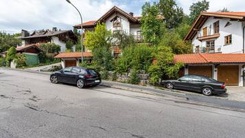 A residential building with a red-tiled roof, a garage, and a street with two parked cars.