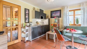 Un espace de vie compact comprenant un coin cuisine, un espace repas avec une table et des chaises, un canapé et un téléviseur fixé au mur.