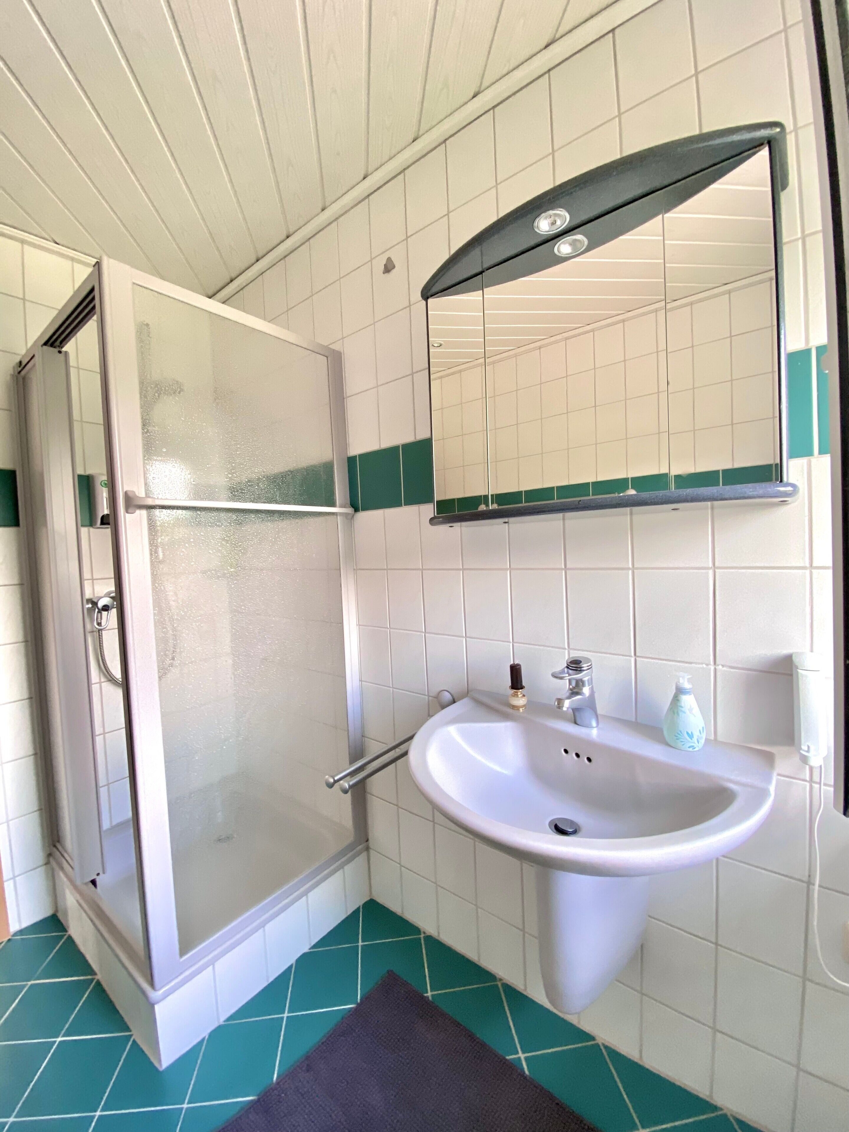 A bathroom with a shower, sink, mirror, and green-tiled floor.