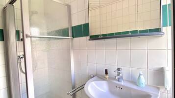 A bathroom with a shower, sink, mirror, and green-tiled floor.
