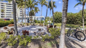 A courtyard with palm trees, picnic tables, and a bicycle. - 🏖🏖 Breathtaking 1 Bedroom ~ Prime Singer Island 🏖🏖 (West Palm Beach)