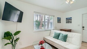A living room with a white sofa, a glass coffee table with a red vase, a flat-screen TV mounted on the wall, and a ceiling fan. - 🏖🏖 Breathtaking 1 Bedroom ~ Prime Singer Island 🏖🏖 (West Palm Beach)