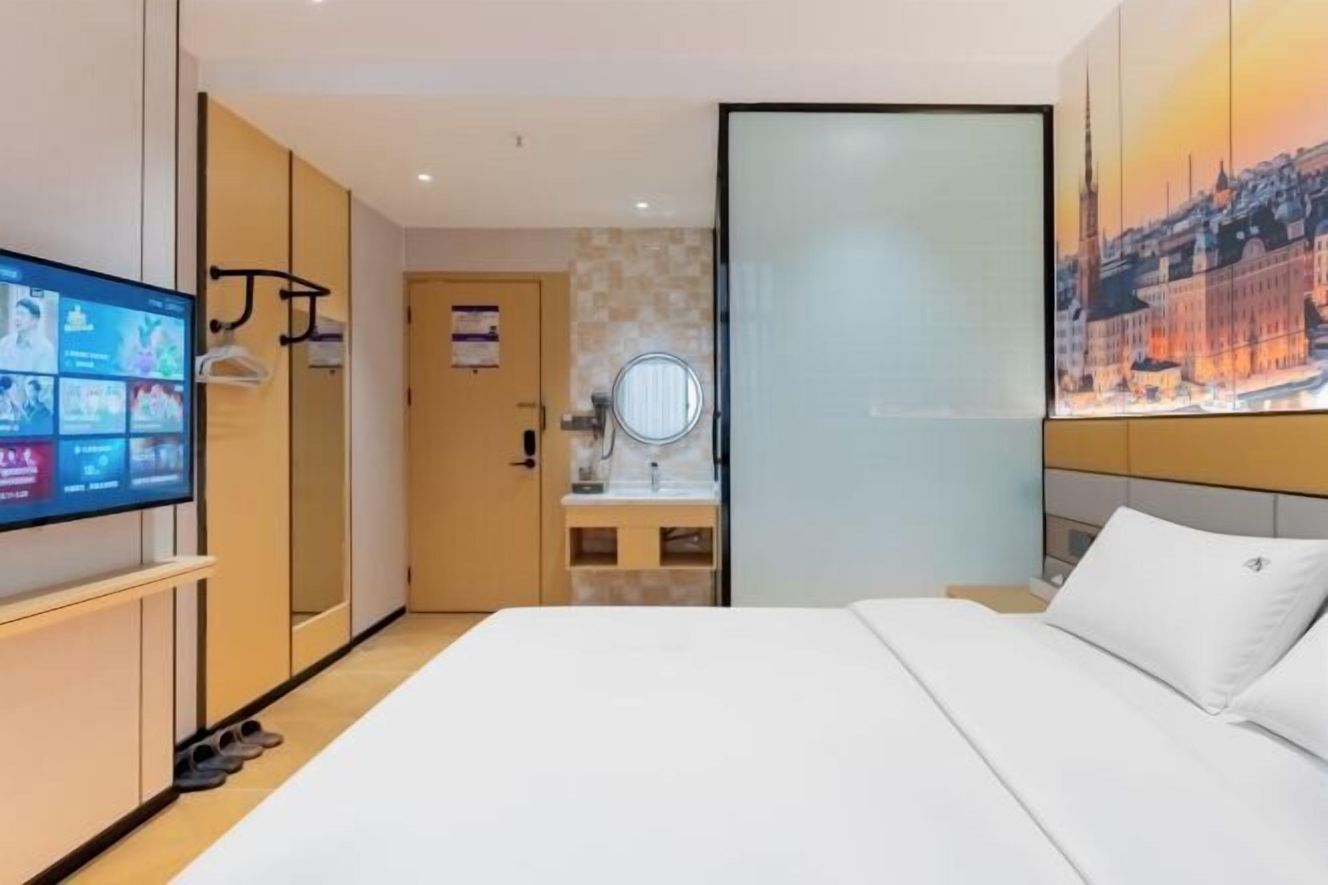 Habitación de hotel con cama, televisión, espejo y una pintura de paisaje urbano.