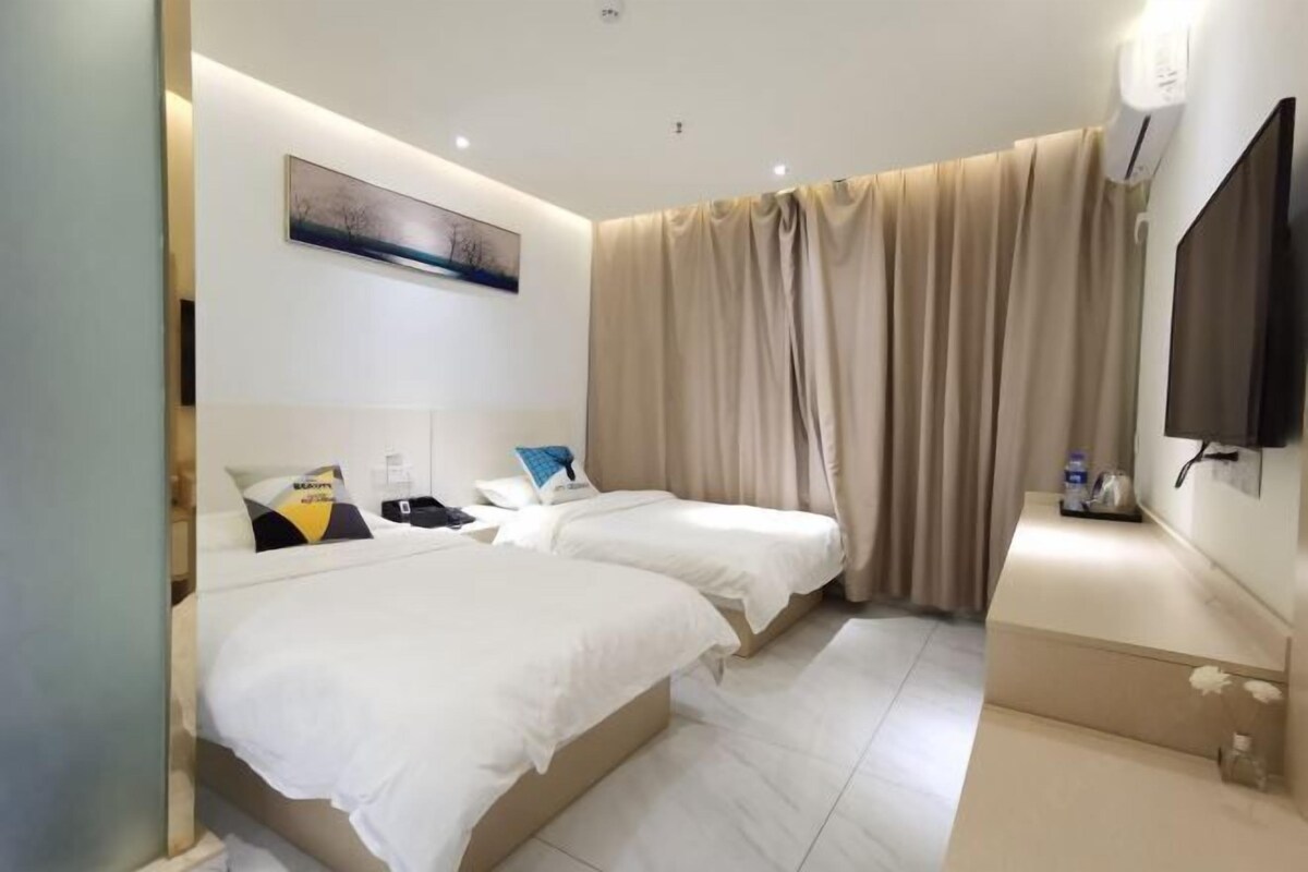 Habitación de hotel con dos camas, un televisor de pantalla plana, un cuadro en la pared y una ventana con cortinas.