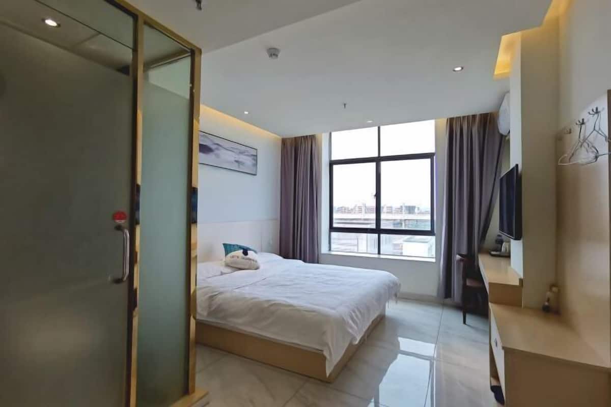 Ein modernes Hotelzimmer mit einem großen Bett, einem Fernseher und einem Fenster mit Vorhängen.