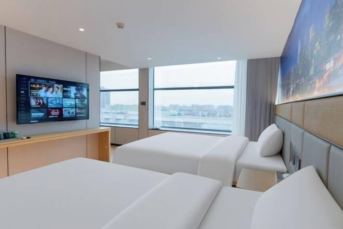 Ein Hotelzimmer mit zwei Betten, einem Fernseher, Blick auf die Stadt und einem Bild an der Wand.