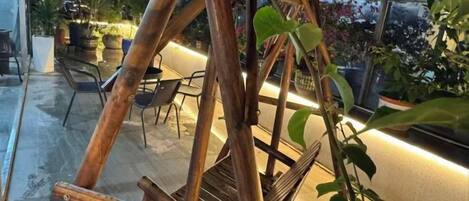 A wooden swing set in an outdoor area with chairs and potted plants.