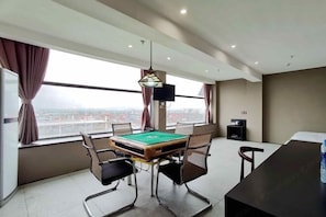 Una habitación de hotel moderna con mesa de billar, asientos cómodos, un ventanal con vistas y un televisor de pantalla plana.