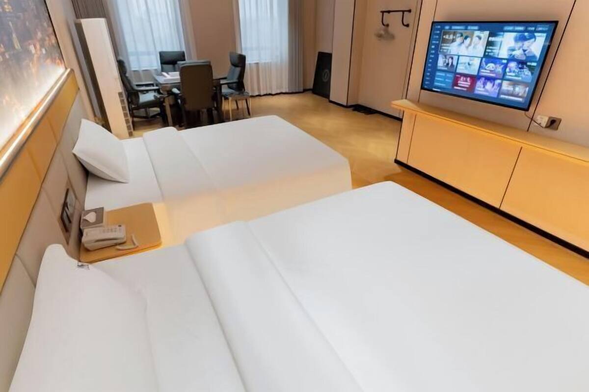 Ein Hotelzimmer mit zwei Betten, einem Schreibtisch, einem Sessel und einem Fernseher an der Wand.