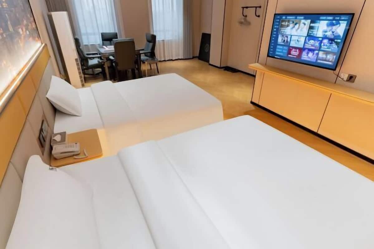 Una habitación de hotel con dos camas, un escritorio, una silla y televisión en la pared.