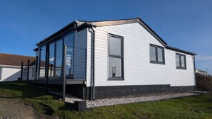 A single-story house with a gable roof, large windows, and a covered porch. - C24 Rosemary, Riviere Towans (Hayle)