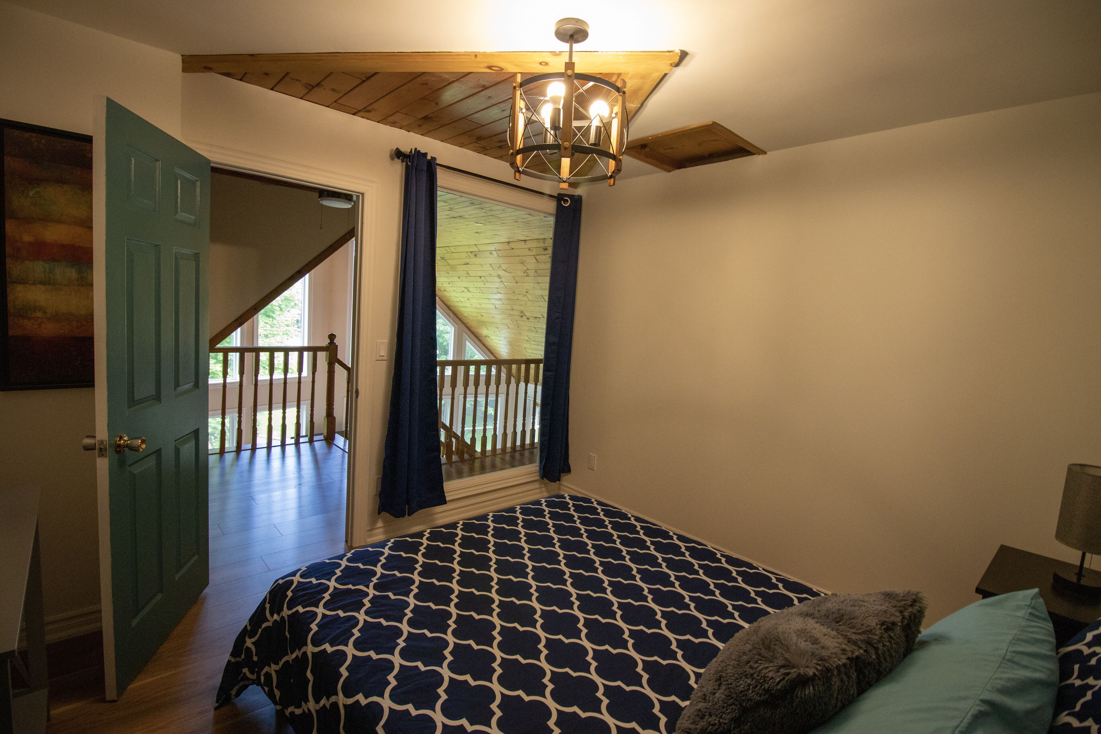 Une chambre à coucher avec une couvre-lit à motifs, un plafond en bois, une vue sur un balcon et une porte donnant sur l’extérieur.