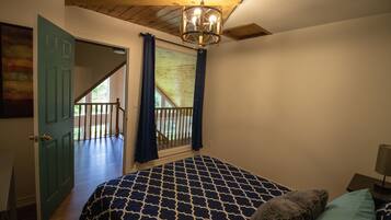 Une chambre à coucher avec une couvre-lit à motifs, un plafond en bois, une vue sur un balcon et une porte donnant sur l’extérieur.
