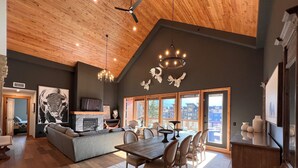 A spacious living area with a fireplace, dining table, and seating. - Iron Mountain Penthouse - World-class Luxury in the Rocky Mountains (Canmore)