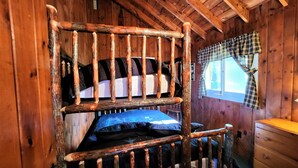 Eine rustikale Holzhütte mit Etagenbett, Karo-Vorhang und Holzkommode.