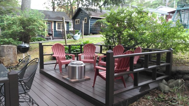 Eine Holzterrasse mit roten Adirondack-Stühlen, einem Metalltisch und einem Grill.