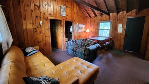 Ein Holzblockhaus-Interieur mit einer Couch, einem gemusterten Sessel, einem Esstisch und einer Tür.