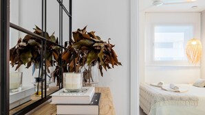 A bedroom with a wooden bedside table, a mirror, a bedside lamp, a bed with a white bedspread, and a view of the sea through the window. - Ground floor with private garden 1min beach (L'Ametlla de Mar)